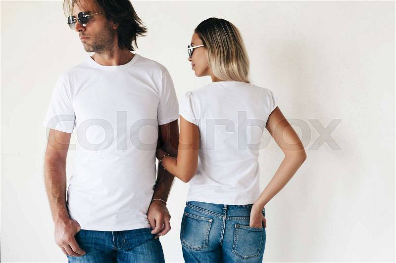 Two hipster models man and woman wearing blanc t-shirt, jeans and sunglasses posing against white wall, toned photo, front and back tshirt mockup for couple, stock photo