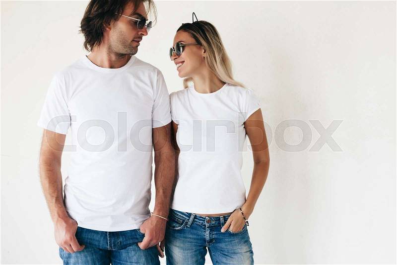Two hipster models man and woman wearing blanc t-shirt, jeans and sunglasses posing against white wall, toned photo, front tshirt mockup for couple, stock photo
