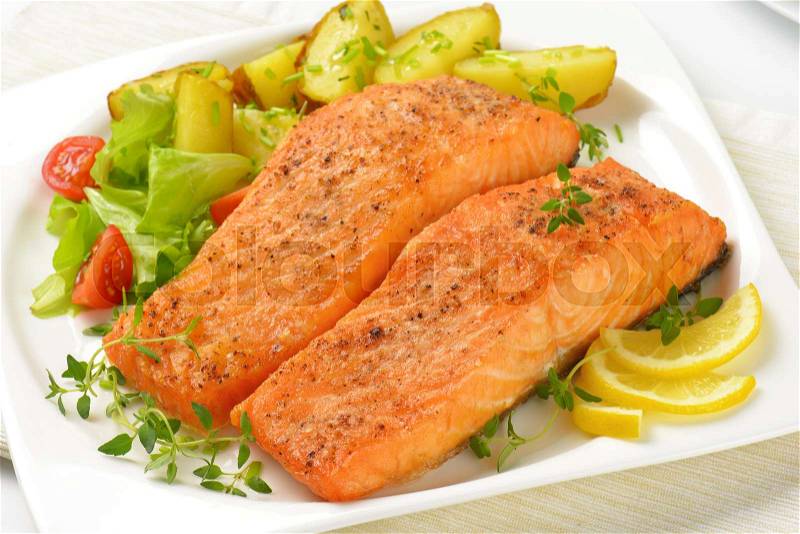 Salmon fillets with roasted potatoes and vegetable garnish on square plate, stock photo