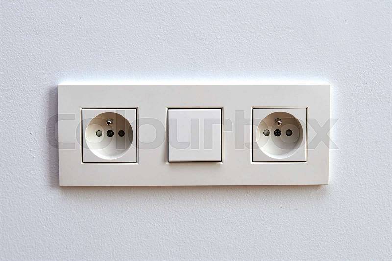 White light switch and electrical outlet in front of white wall, stock photo