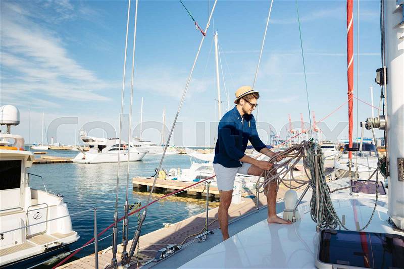 Young stylish sailor man in hat and sunglasses standing on the yacht, stock photo