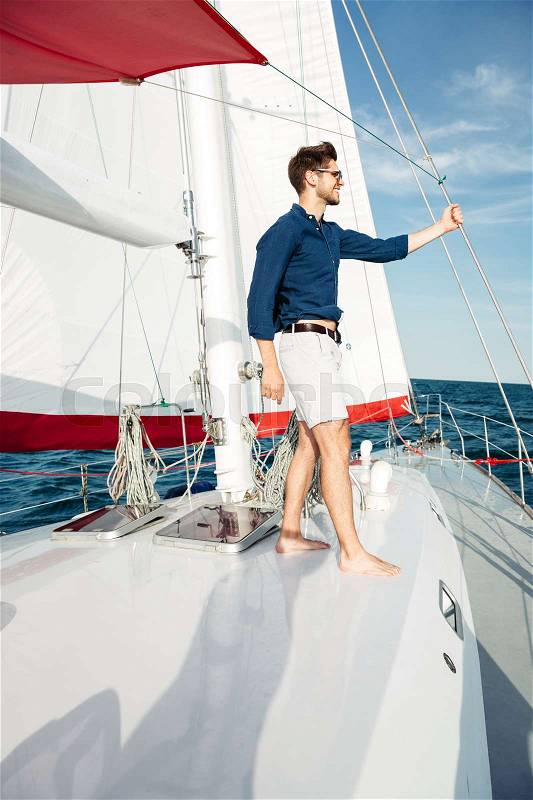 Young bearded man standing on a yacht and looking at the horizon, stock photo