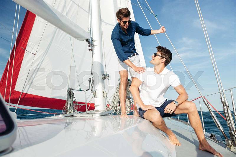 Two young handsome happy men talking while standing on the yacht, stock photo