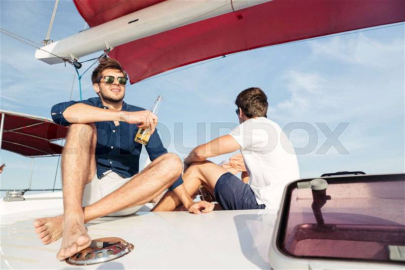 Two young handsome men friends drinking beer while resting on the yacht, stock photo