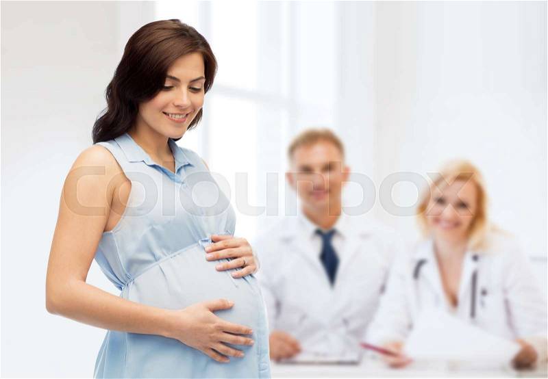 Pregnancy, motherhood, people, medicine and fertility concept - happy pregnant woman touching her big belly over medics at maternity hospital background, stock photo