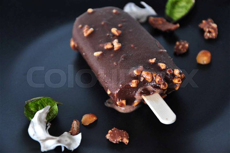Close up chocolate ice cream bar with nuts melting on black plate, stock photo