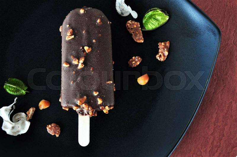 Close up chocolate ice cream bar with nuts on black plate, stock photo