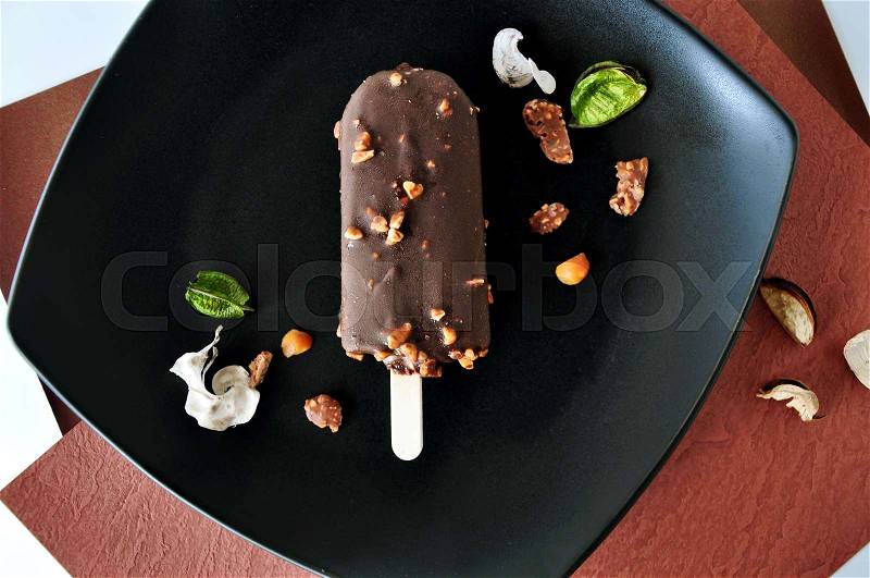 Top view of chocolate ice cream bar with nuts on black plate, stock photo