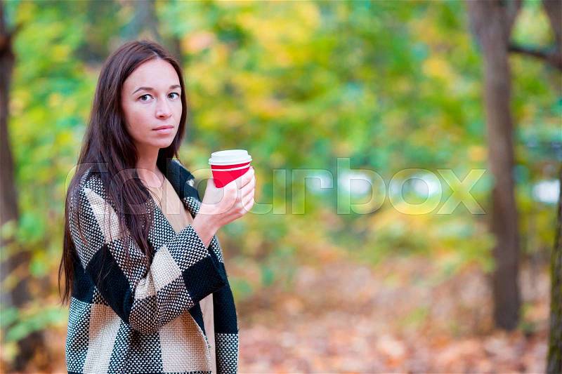 Beautiful woman drinking coffee in autumn park under fall foliage. Coffee to go in her hands, stock photo