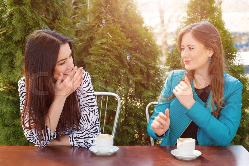 Communication and friendship concept -two girls drinking coffee in a coffee shop terrace looking each other, stock photo