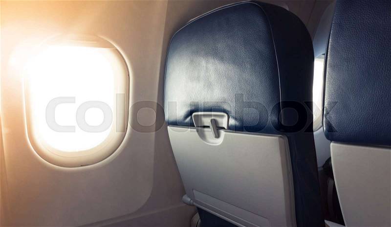 Passenger plane interior fragment. Main cabin chairs with folding table and glowing porthole with natural sunlight lens flare, stock photo