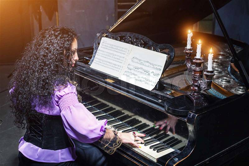 Mystic woman playing the piano, candles on the piano, stock photo