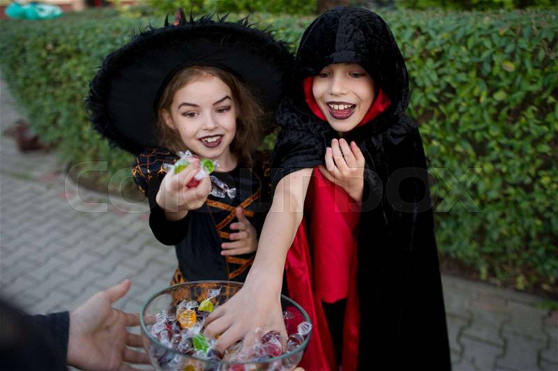 Boy and girl in black suits for Halloween take candies from a vase. On the children\'s faces frightening make-up. Children delighted with the event, stock photo