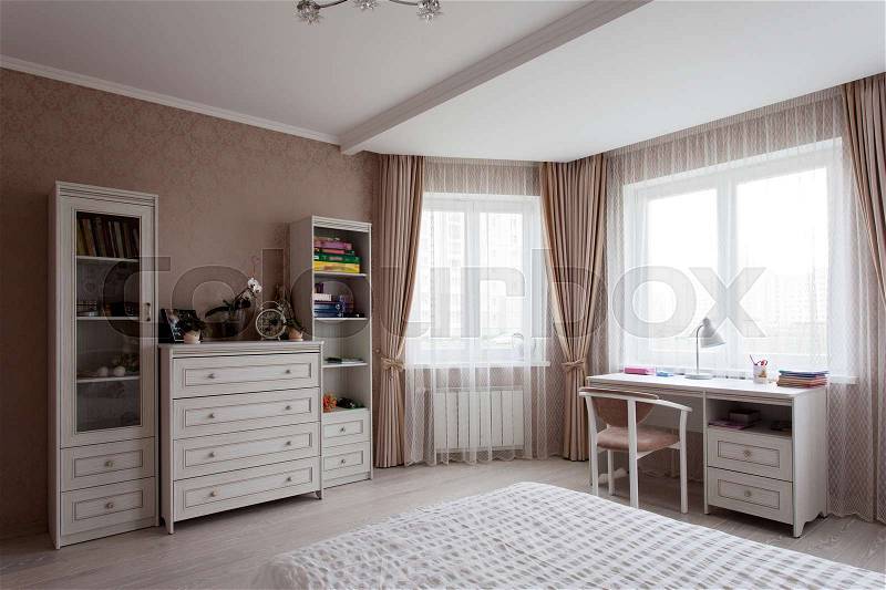 White chest of drawers, bad and a writing desk near the window in a room, stock photo
