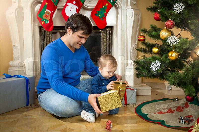 Young father and cute baby son opening Christmas gifts on floor at living room, stock photo