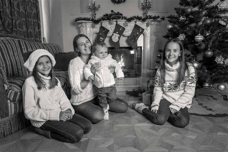 Black and white image of happy big family sitting on floor at fireplace on Christmas, stock photo