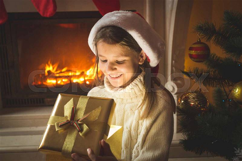 Portrait of cheerful 10 years old girl looking inside of magical glowing Christmas gift box, stock photo
