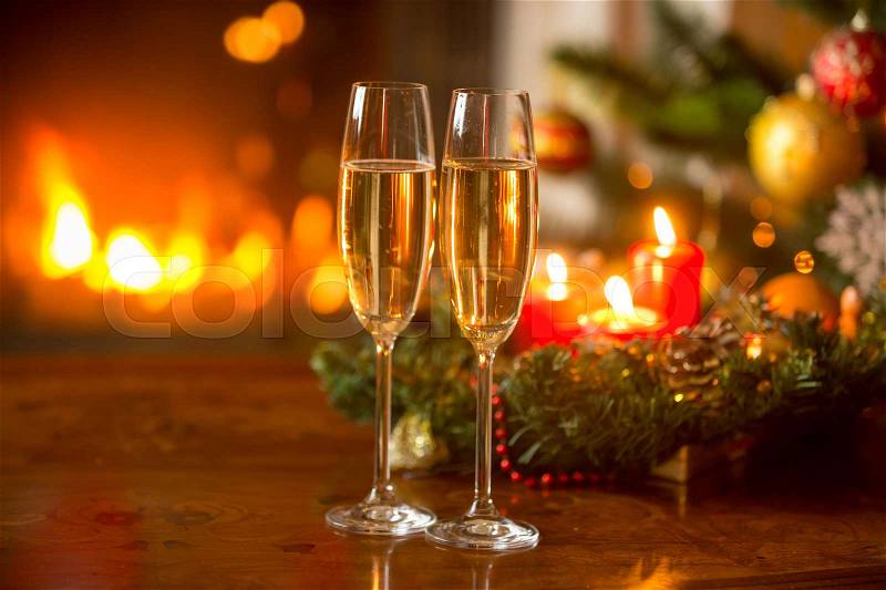 Beautiful Christmas background with two champagne flutes, burning fireplace and wreath with candles, stock photo
