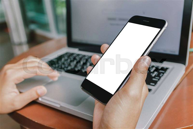 Hand holding phone and using laptop computer in coffee shop, stock photo