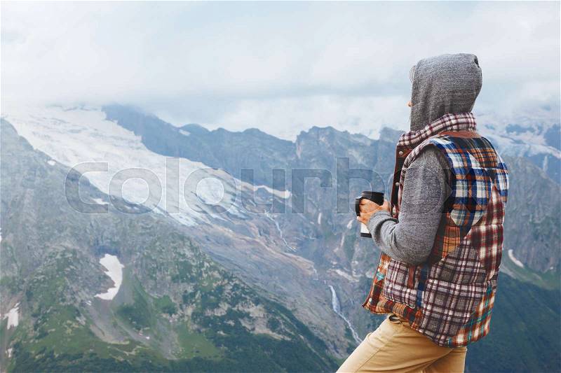 Man drinking hot coffee in thermos mug and looking into the mountains in snow, winter hike, cold season, stock photo