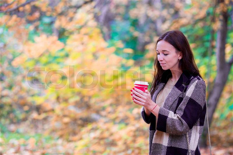 Beautiful woman drinking coffee in autumn park under fall foliage. Coffee to go, stock photo