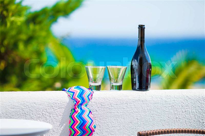 Glasses, bottle of tasty wine and swimsuit on balcony in greek island with view of sea, stock photo