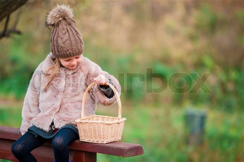 Adorable little girl with a basket in autumn day outdoors, stock photo