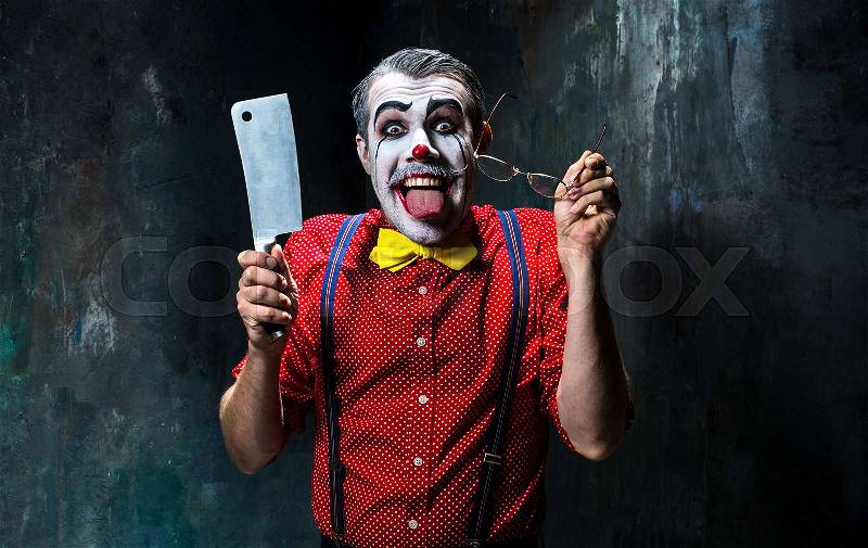 The scary clown holding a knife on dack. Halloween concept of horror and murderer, stock photo