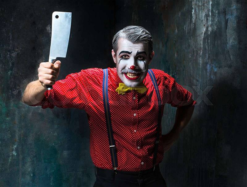 The scary clown holding a knife on dack. Halloween concept of horror and murderer, stock photo