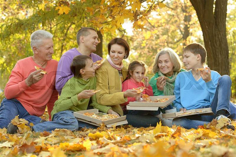 Happy family eat pizza together in autumn park, stock photo