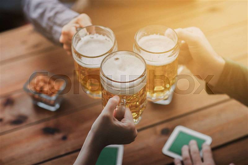 People, leisure and drinks concept - close up of hands clinking beer mugs at bar or pub, stock photo