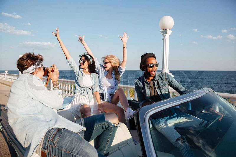 Group of happy young people taking photos and having fun in cabriolet, stock photo