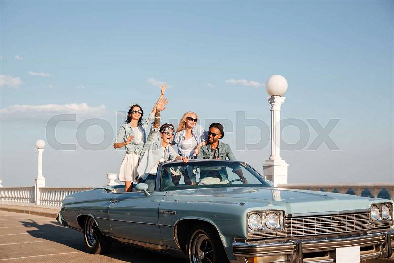 Group of smiling young people driving old vintage cabriolet car, stock photo