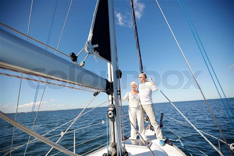 Sailing, age, tourism, travel and people concept - happy senior couple hugging on sail boat or yacht deck floating in sea, stock photo