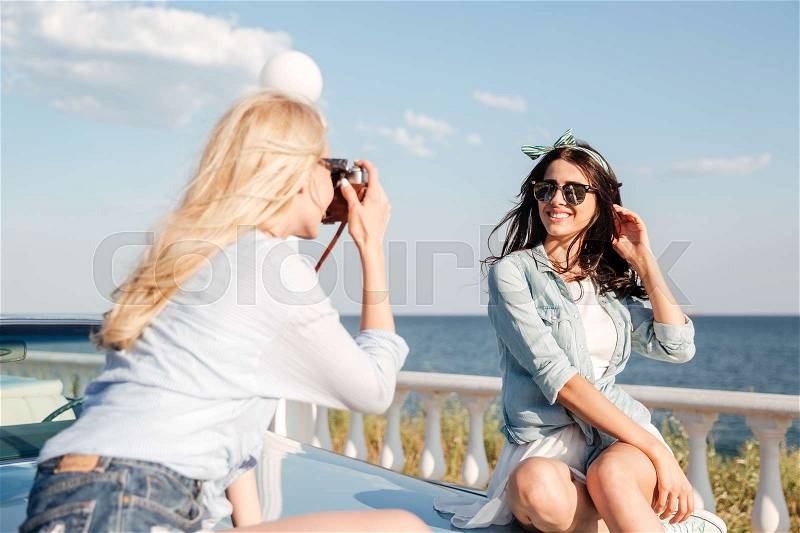 Cheerful attractive young woman sitting and posing to girl photographer in summer, stock photo