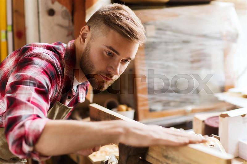 Profession, carpentry, woodwork and people concept - carpenter testing wood plank evenness at workshop, stock photo