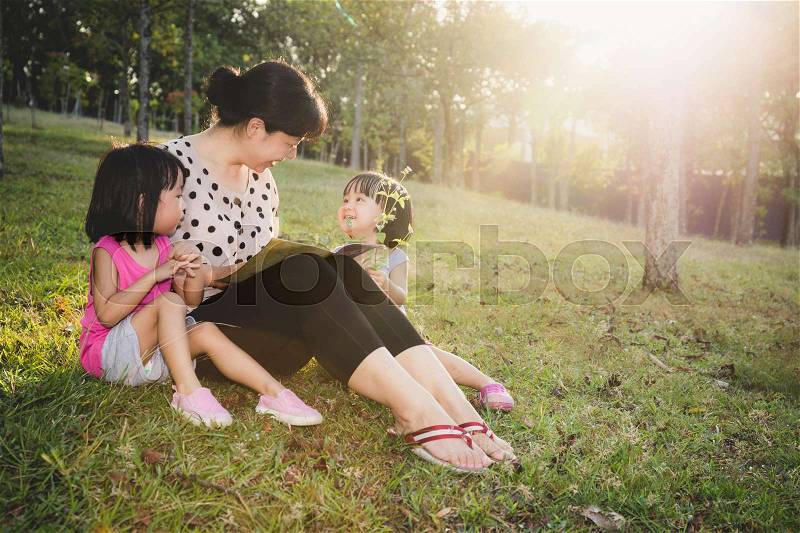 Asian Chinese Mother and Daughters Reading at outdoor Park, stock photo