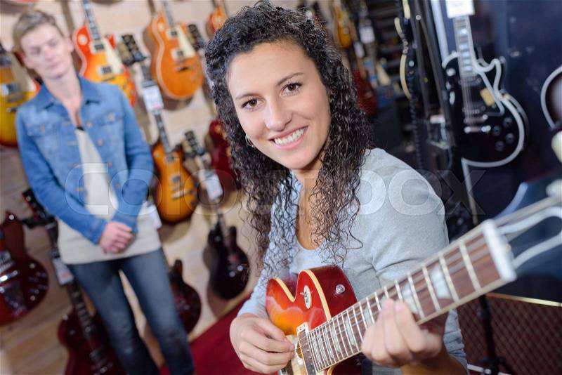 Woman trying electric guitar in store, stock photo