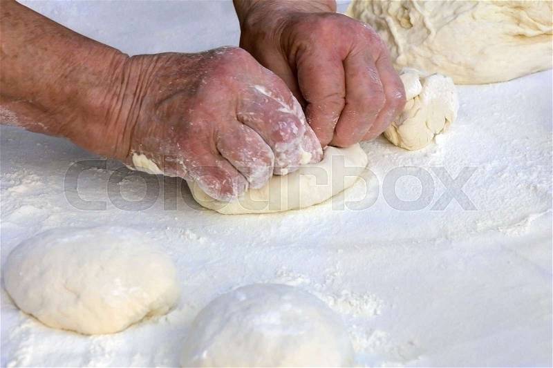 Older woman hands knead dough on a table in her home kitchen , stock photo