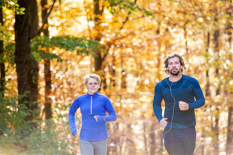 Beautiful couple running together outside in sunny autumn forest, stock photo
