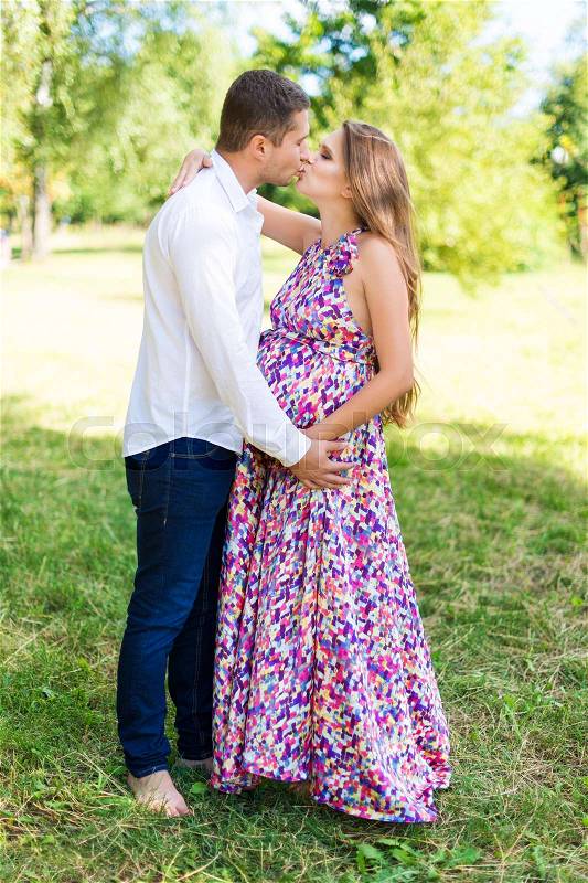 Beautiful pregnant couple happy together expecting a child. Man and woman kissing while walking in the park. Share the love, family, love concept, stock photo