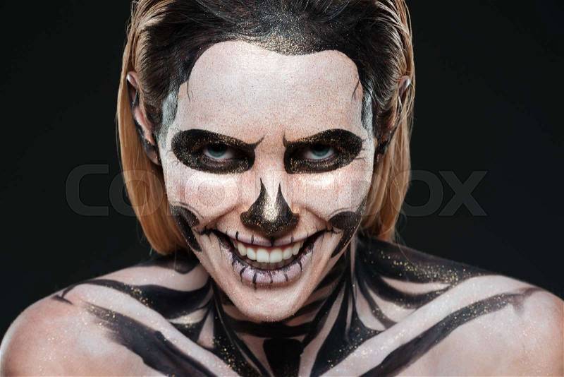 Smiling young woman with skeleton halloween makeup laughing over black background, stock photo