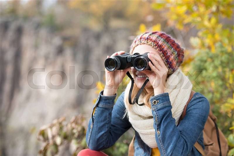 Beautiful woman looking through binoculars against colorful autumn forest, stock photo