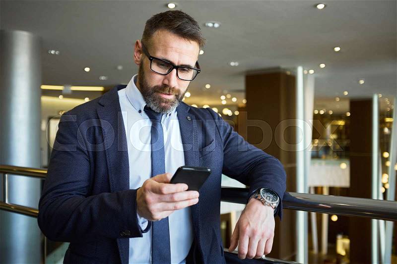 Mature businessman reading sms in business center, stock photo