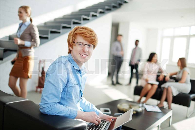 Happy young man looking at camera in working environment in office, stock photo