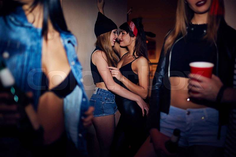 Sneak shot of two drunk sexy girls flirting and caressing each other in dark corner of nightclub at noisy party, stock photo