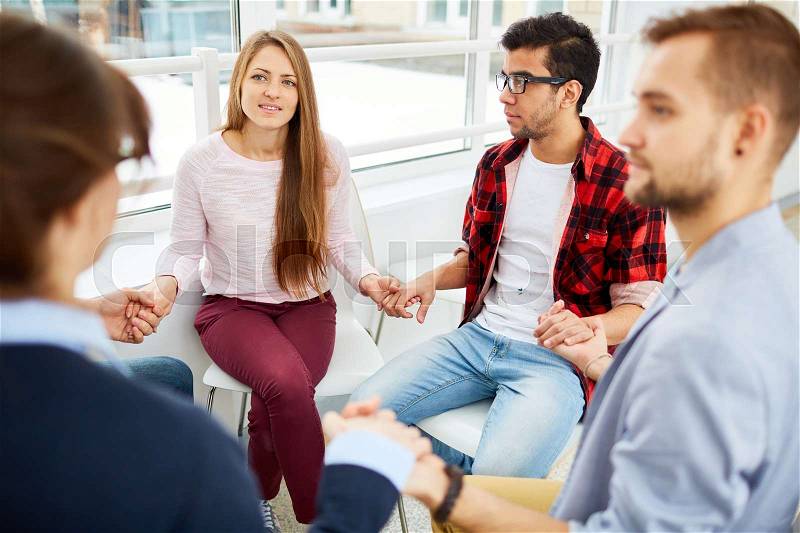 Group of guys and girls holding by hands during psychological session, stock photo
