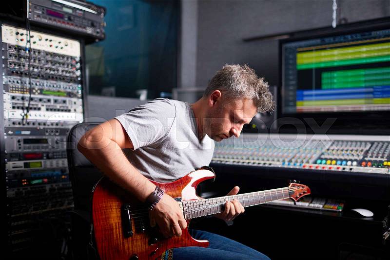 Greyhaired man playing guitar in audio studio, stock photo