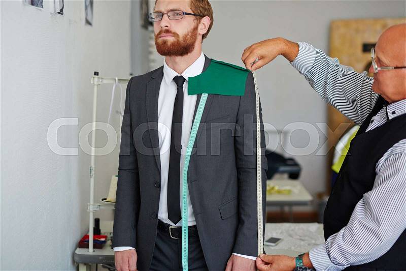 Tailor measuring length of jacket sleeve worn by man, stock photo