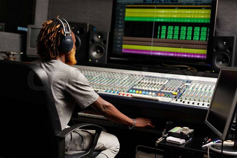 Sound producer sitting by mixing equipment in studio, stock photo